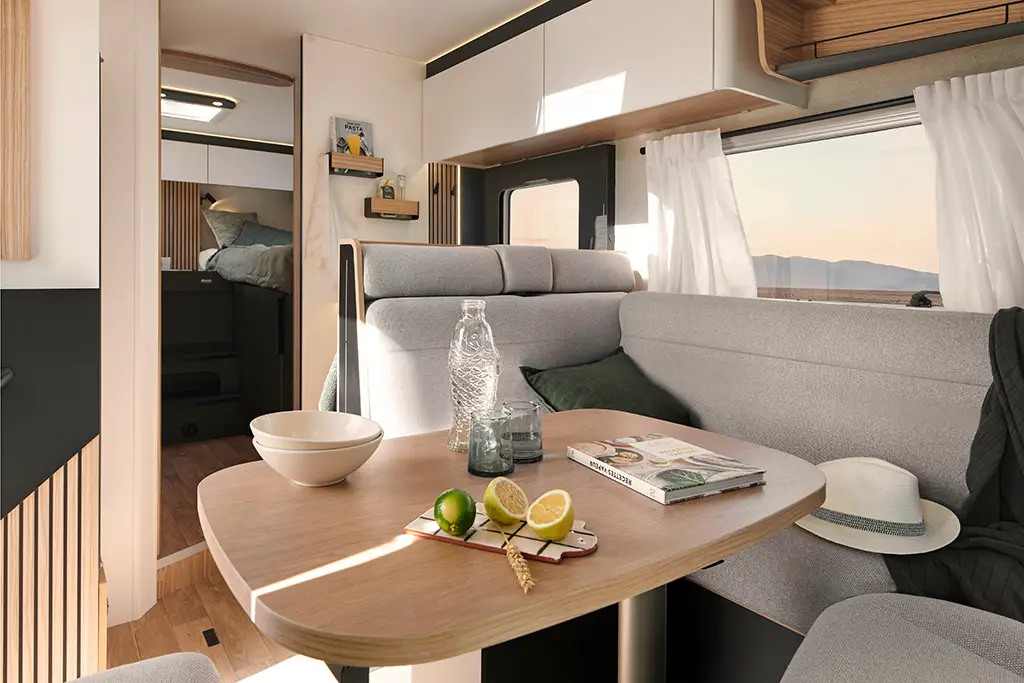 Intérieur d'un camping car intégral avec banquette en tissu clair et table en bois.