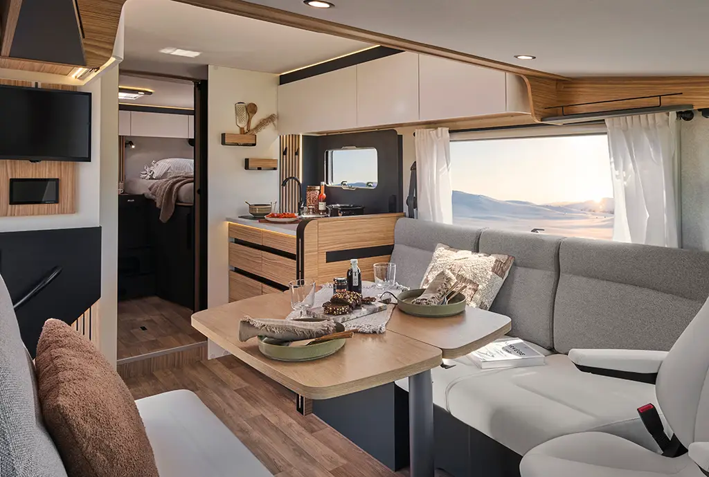 Intérieur d'un camping car intégral avec banquette en tissu clair, table en bois et rangement