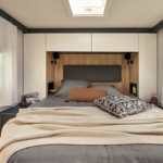 Chambre arrière d'un camping car profilé avec un grand lit et des placards haut.