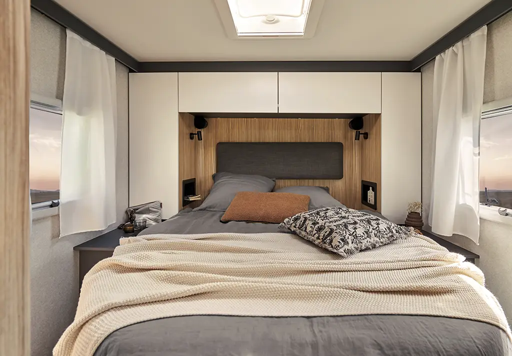 Chambre arrière d'un camping car profilé avec un grand lit et des placards haut.