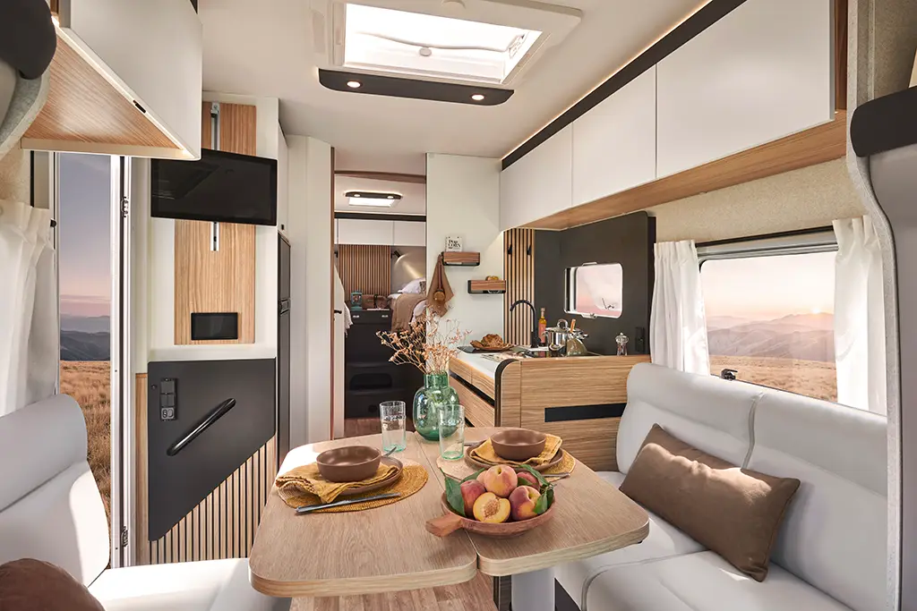 Intérieur d'un camping car profilé avec banquette en tissu clair, table en bois et placards hauts.