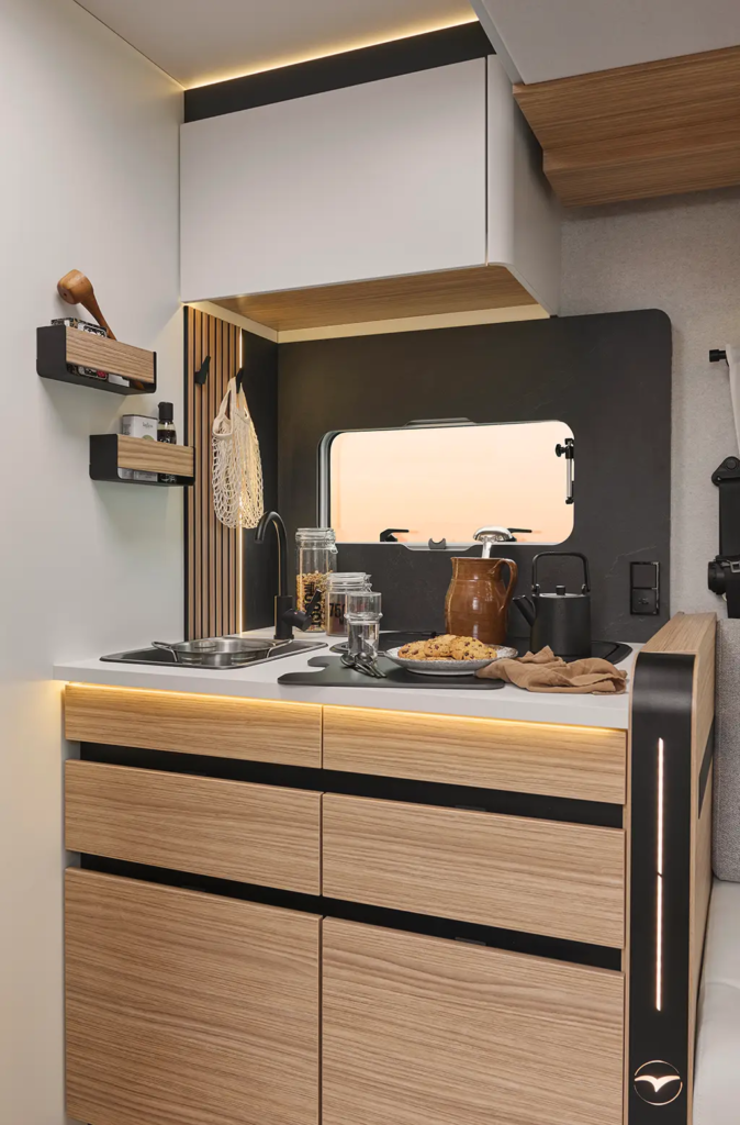 Espace cuisine d'un camping car profilé comprenant un évier en inox et des rangements intégrés.