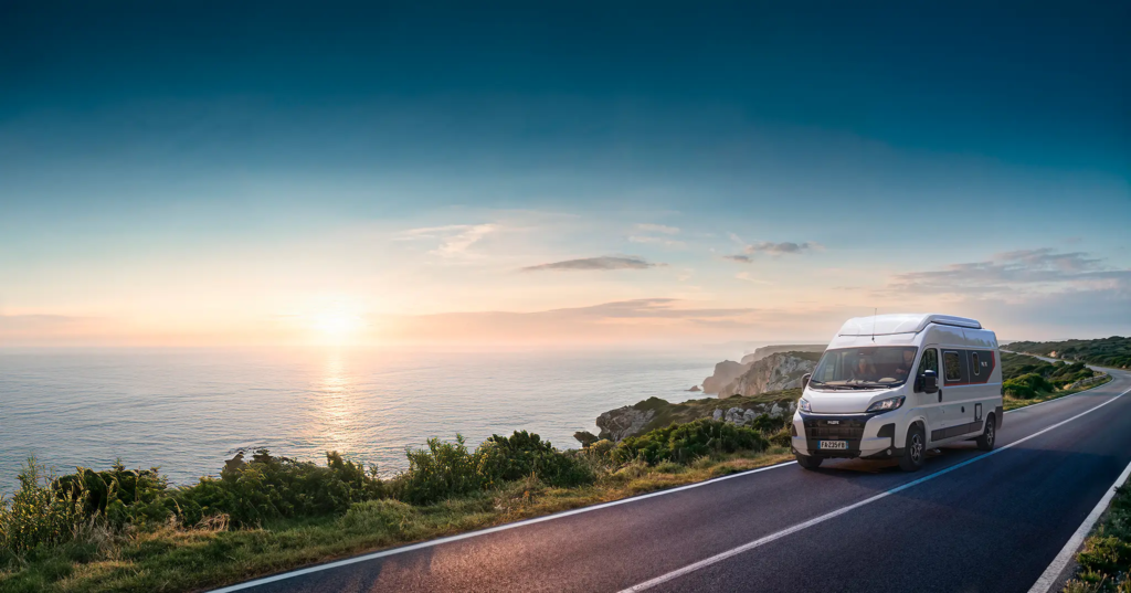 Fourgon aménagé V600G roulant sur une route au bord de mer au soleil couchant