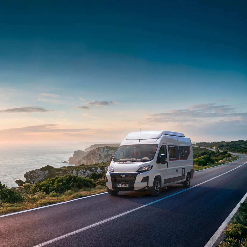 Fourgon aménagé V600G roulant sur une route au bord de la mer au soleil couchant